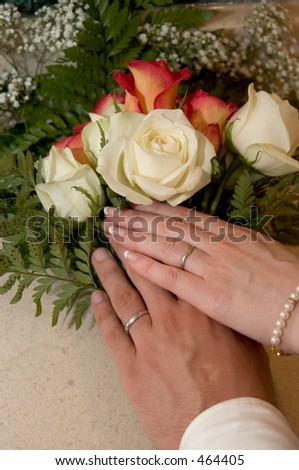 Brides and groom hands showing wedding rings on top of a bouquet.
