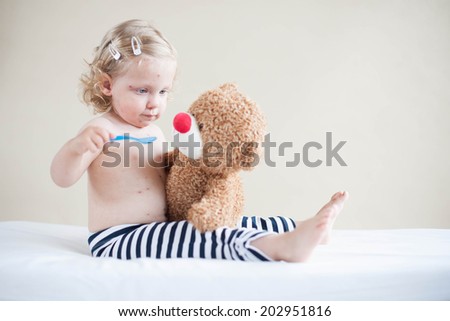 Sick girl is feeding teddy-bear on the bed