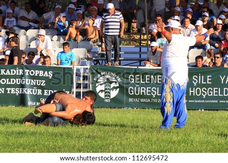 ISTANBUL - AUGUST 24: Unidentified wrestlers in the 8th Sile Annual Oil Wrestling Event on August 24, 2012 in Istanbul. Judge standing by two competitors wrestle