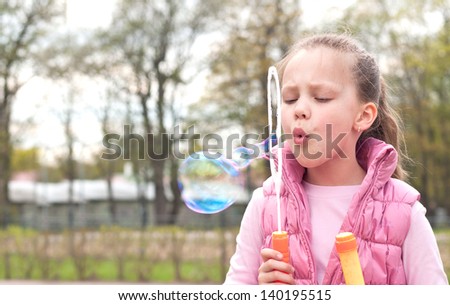 young girl inflates soap bubbles in the park
