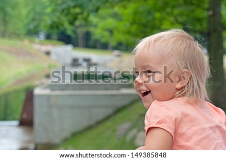 the child looks to the side, standing on a bridge in the park