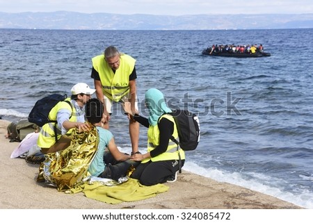 LESVOS, GREECE - SEPTEMBER 29, 2015: Refugee given help after being brought ashore by a volunteer lifeguard. A refugee boat and Turkey seen in the background.