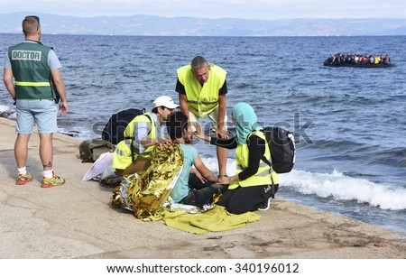 LESVOS, GREECE - SEPTEMBER 29, 2015: Refugee given help after being brought ashore by a volunteer lifeguard. A refugee boat and Turkey seen in the background. These Syrians are escaping from war & IS.
