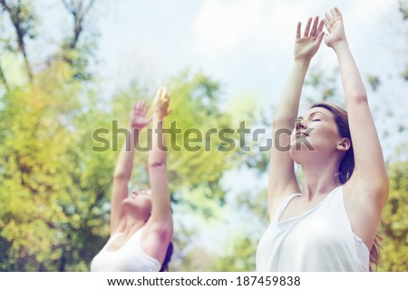 Two beautiful young women doing yoga class in nature.