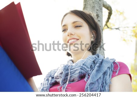 Beautiful happy young woman sitting on grass, enjoy sunny day and listening music with headphones while reading book. Happy young woman sitting on grass and reading a book.