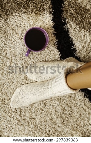 Image of legs crossed on carpet, resting, wearing woolen socks. Show of enjoyment in the morning