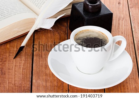 cup of coffee with a quill pen and inkwell on wooden background book