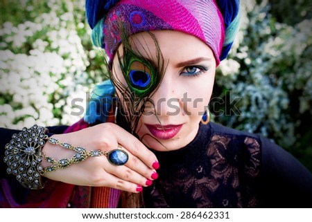 beautiful girl in a turban with a peacock feather in her hands on the flowers of spirea background