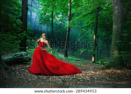 A girl in a long red dress and a royal crown in the forest