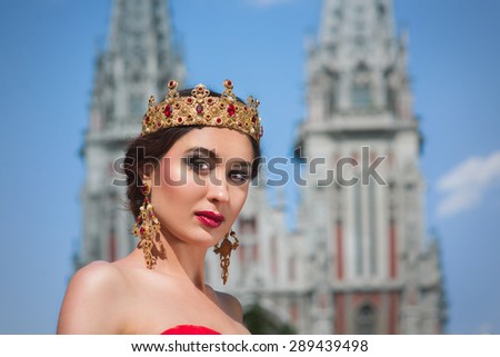 A beautiful girl in a long red dress and a royal crown in the catholic church\'s background