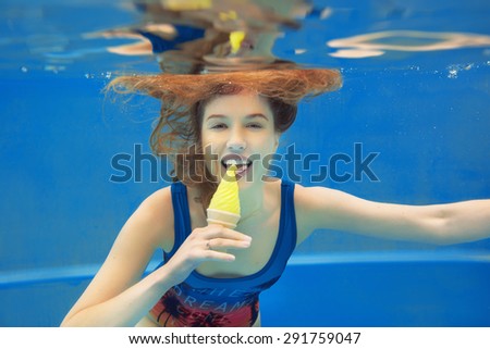 Beautiful smiling red hair girl eating yellow ice cream in the swimming pool underwater in summer