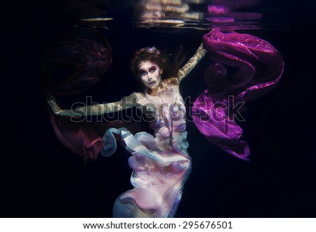 girl in colorful clothes on the dark background swimming underwater