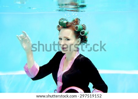 young girl in a bathrobe and curlers  underwater in the swimming pool
