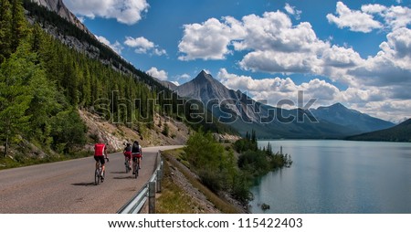 Three cyclists on a road in Jasper national park with a mountain peak in the distance.