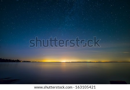 Distant city lights over water with stars