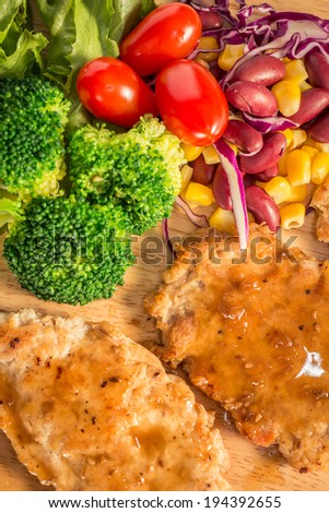 Pork cube steak topped with pepper sauce and creamy salad on wood plate