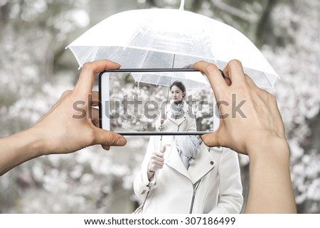 Girl taking pictures on mobile smart phone at Japanese woman with cherry blossoms on a rainy day.