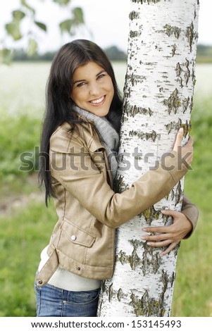 Happy woman put her arms around a birch tree