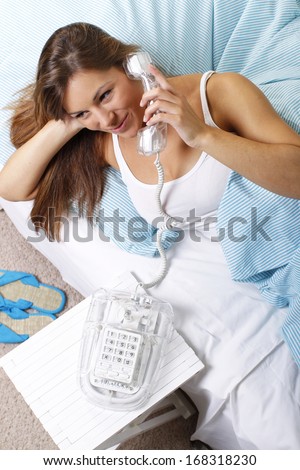 Smiling young woman in bed with old cord telephone