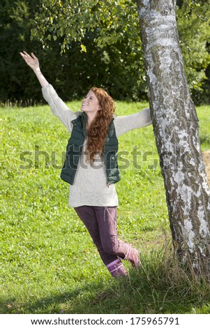 Attractive woman holds a birch tree and stretches her arm to the sky