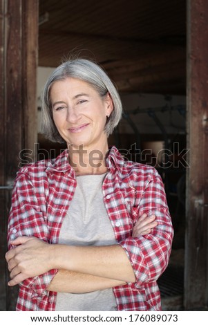 Matured farm woman with crossed arms in front of a barn smiling