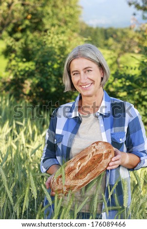 Matured farm woman with freshly baked bread in front of a corn field