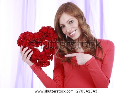 Happy smiling woman pointing at rose flower heart