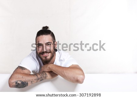 Friendly young tattoo man with pony tail leaning across a white wall