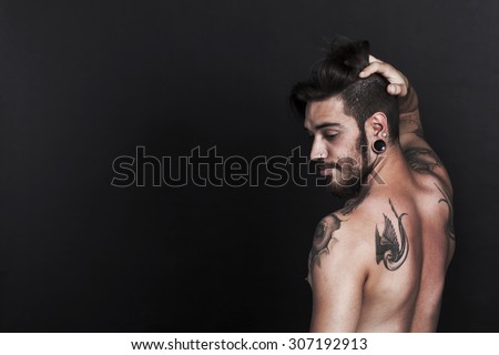 Serious young urban man with tattoo looking sideways with black background