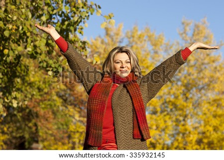 Happy middle aged woman with arms outstretched in autumn