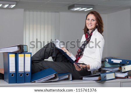 Attractive businesswoman sits on a desk surrounded by stacks of files