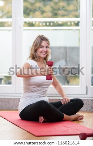 Young fair-haired woman trains with a dumb bell on a gymnastic mat