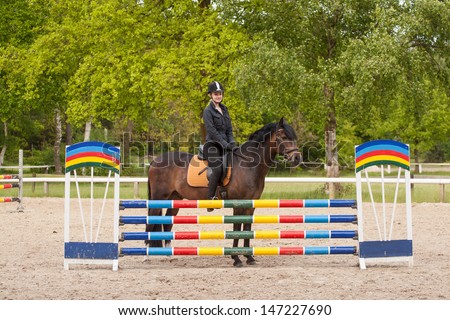 Girl jumps with her brown horse (New-Forest-Pony) over an obstacle