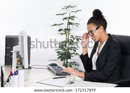 Young, beautiful office worker sits at the desk in the office and looks concentrated at the monitor