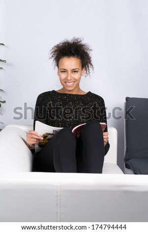 Young, beautiful woman sits on the couch and reads a magazine in the free time.