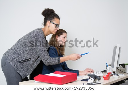 Two business women in front of the computer in the office. Both women are looking to the monitor. One woman is pointing to the monitor.