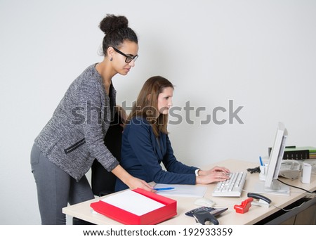 Two business women in front of the computer in the office. Both women are looking to the monitor.
