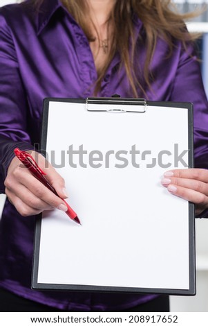 A businesswoman is pointing to a clipboard holding a white sheet of paper with a red pen.
