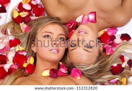 Beautiful blonde sisters twins lying in red rose  petals