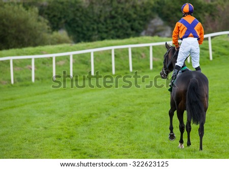 jockey standing up on race horse riding down the track