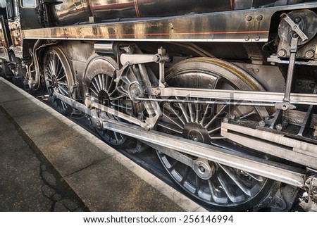 Old steam engine wheels beneath a steam train