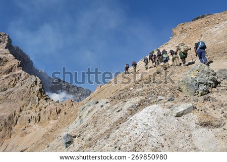 KAMCHATKA, RUSSIA - SEPTEMBER 11, 2013: Group of tourists climbing on the steep slope to the active crater Mutnovsky Volcano. Kamchatka Peninsula, Russia, Far East.