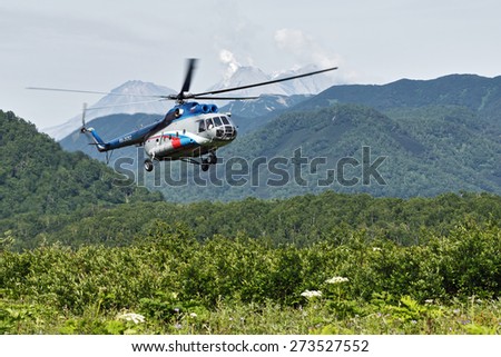 KAMCHATKA, RUSSIA - JULY 11, 2014: A russian helicopter MI-8 with tourists flying in the forest on the background of mountains and volcano sunny summer day. Kamchatka Peninsula, Far East, Russia.