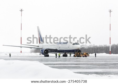PETROPAVLOVSK-KAMCHATSKY, KAMCHATKA, RUSSIA - MARCH 19, 2015: Airdrome trucks pulling airplane Boeing-767 Transaero Airlines at airport of Petropavlovsk-Kamchatsky during a snowfall, poor visibility.