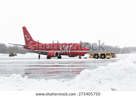 PETROPAVLOVSK, KAMCHATKA, RUSSIA - MARCH 19, 2015: Airdrome trucks pulling airplane Boeing 737-500, Aurora Airlines at airport of Petropavlovsk-Kamchatsky during a snowfall and poor visibility.