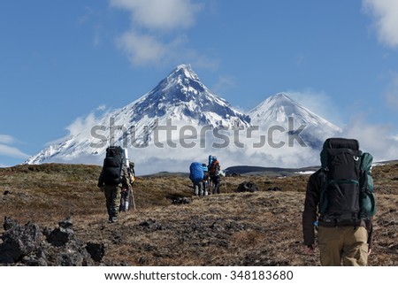Hikers group trekking in Kamchatka mountain on background of Klyuchevskaya group of volcanoes: Kamen, active Klyuchevskoi Volcano, active Bezymianny Volcano. Russia, Far East, Kamchatka Peninsula.