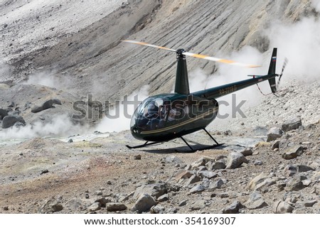 MUTNOVSKY VOLCANO, KAMCHATKA, RUSSIA - JULY 4, 2014: Touristic Helicopter Robinson R44 Raven with tourists on board standing by in crater active Mutnovsky Volcano on background of steaming fumaroles.