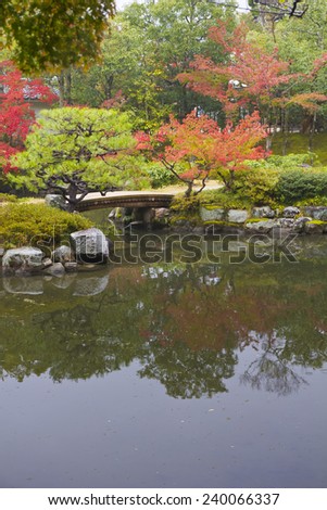 Colorful autumn trees on a garden with water reflection lake and small bridge path.