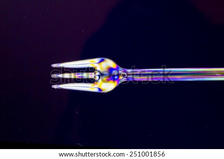 Isolated transparent polarized fork on a lighting technique on a black background.