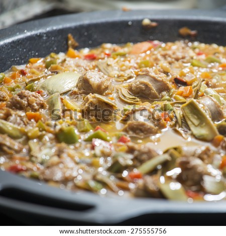 Spanish paella, typical Mediterranean food made of rice, vegetables and meat being cooked on a black pan in a domestic kitchen.